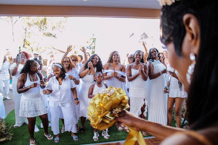 Guests cheering as a bride holds a gold bouquet in the foreground