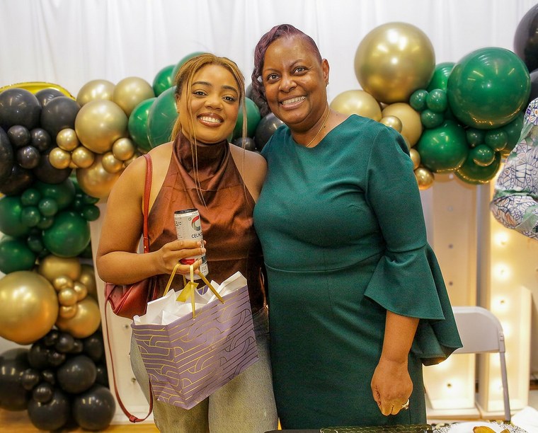 Two guests smiling beside green and gold balloons at a retirement celebration